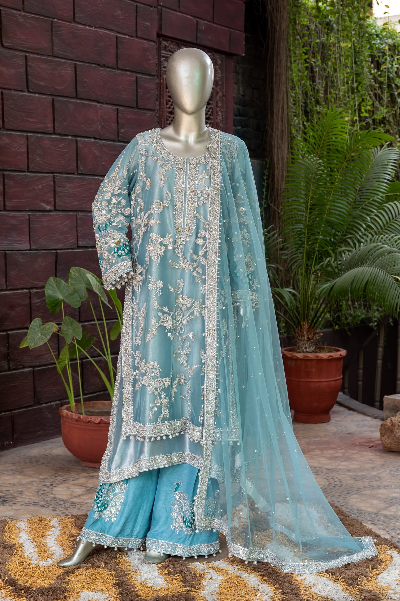 Teal Pakistani formal suit by MariamRaj featuring hand-embellished net shirt with zari, mirror work, pearls, and sequins, paired with tissue inner, embroidered pants, and a net dupatta.