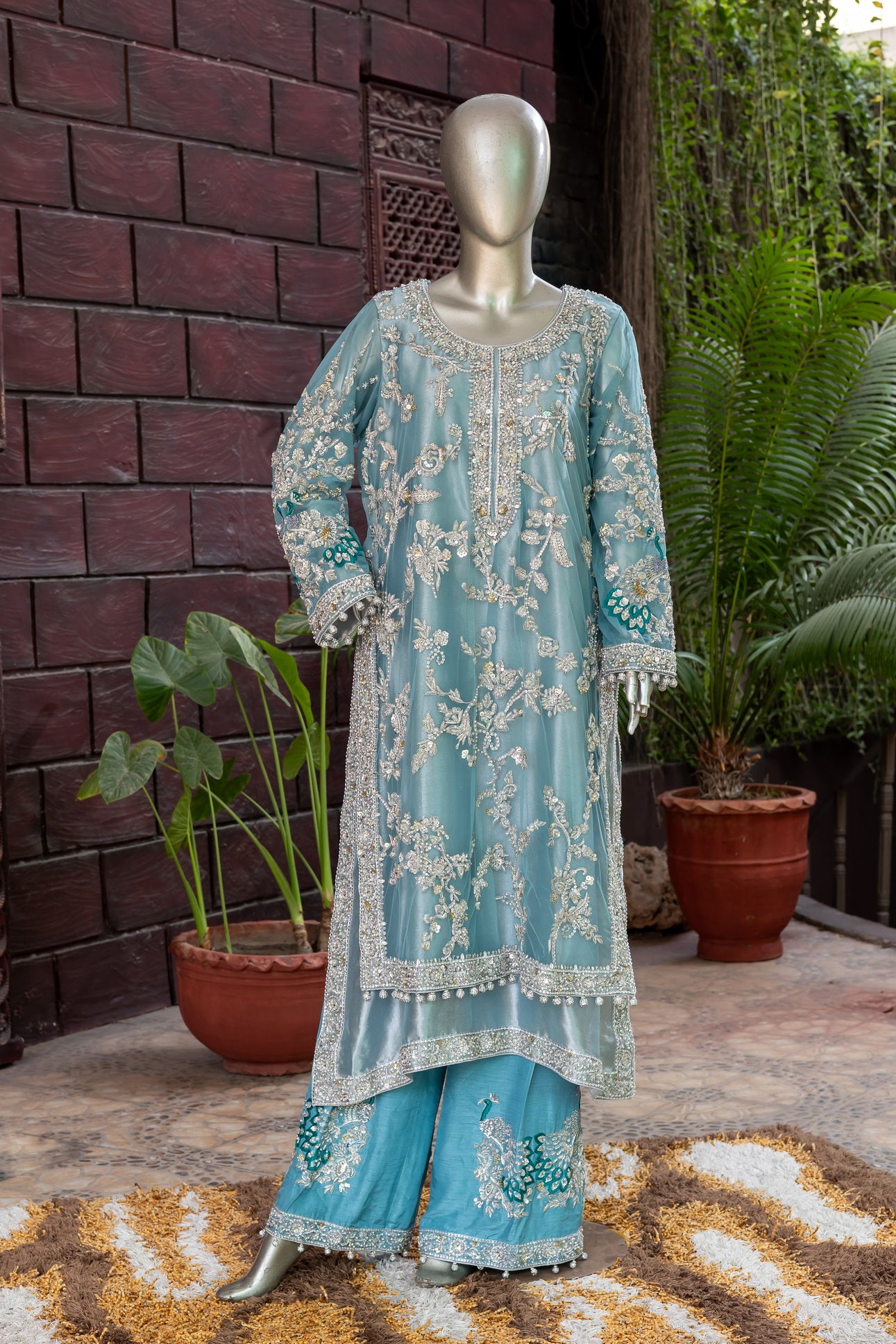 Teal Pakistani formal suit by MariamRaj featuring hand-embellished net shirt with zari, mirror work, pearls, and sequins, paired with tissue inner, embroidered pants, and a net dupatta.