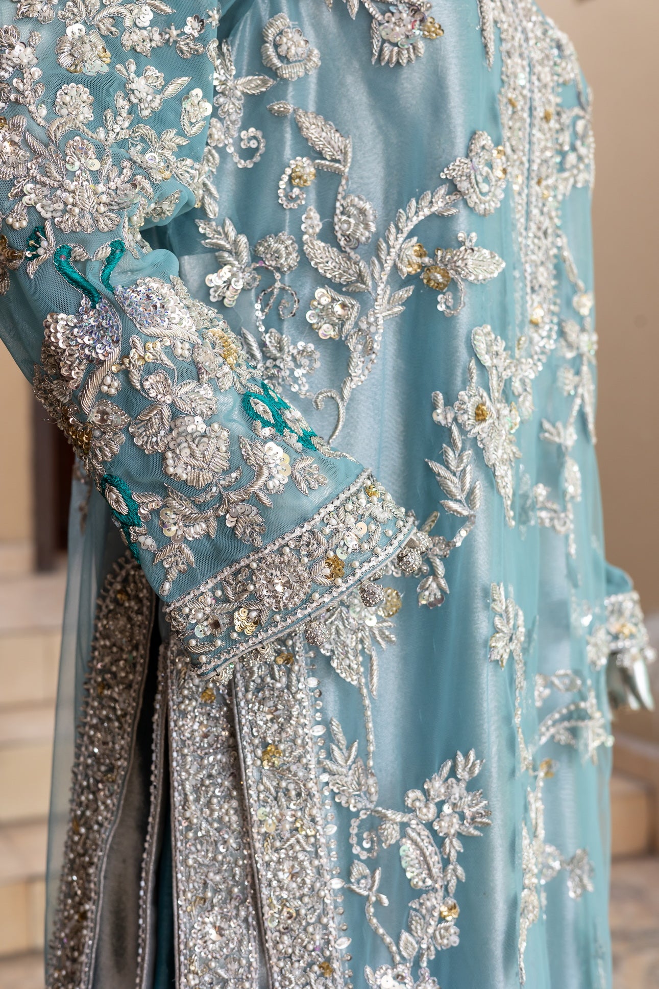 Teal Pakistani formal suit by MariamRaj featuring hand-embellished net shirt with zari, mirror work, pearls, and sequins, paired with tissue inner, embroidered pants, and a net dupatta.