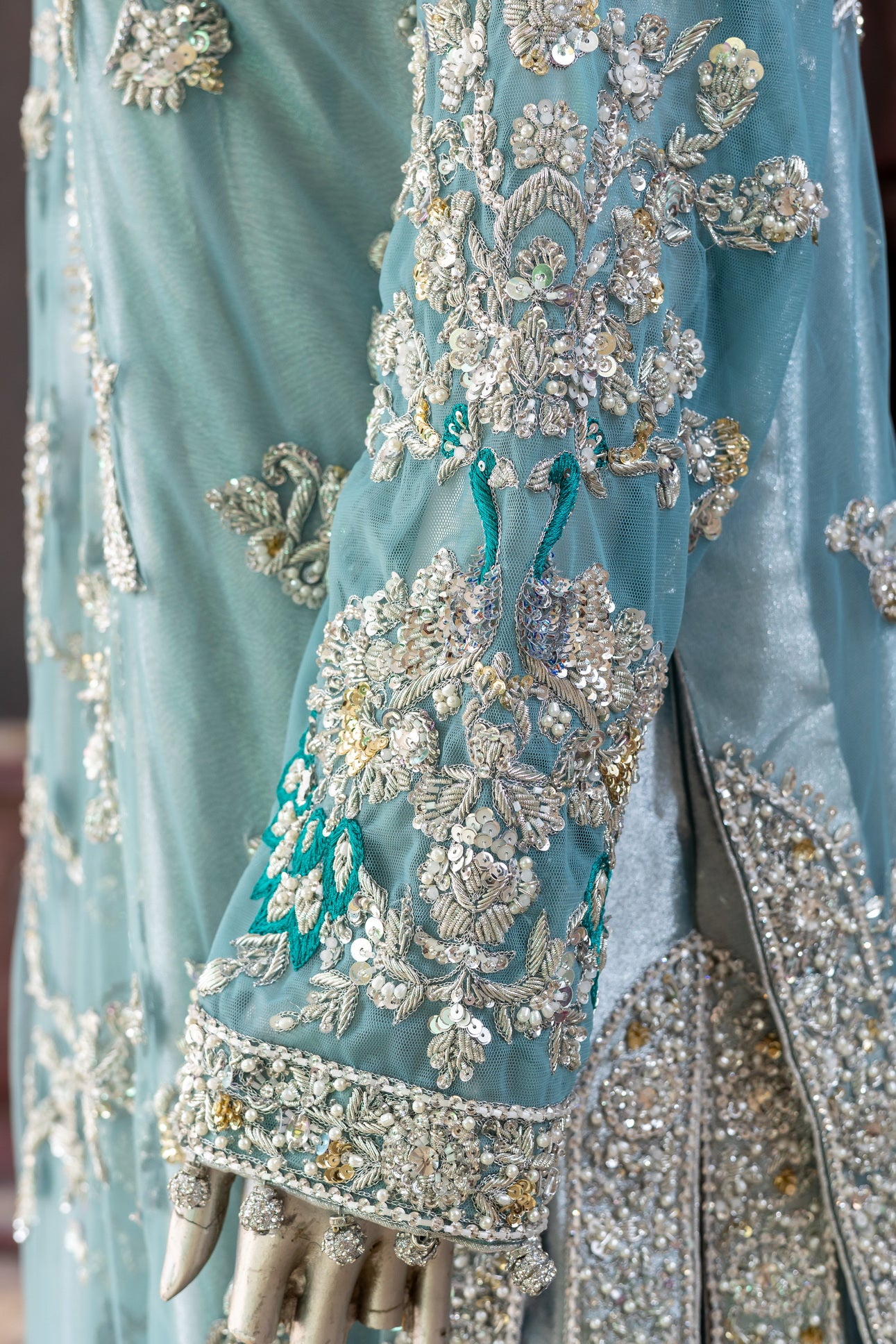Teal Pakistani formal suit by MariamRaj featuring hand-embellished net shirt with zari, mirror work, pearls, and sequins, paired with tissue inner, embroidered pants, and a net dupatta.