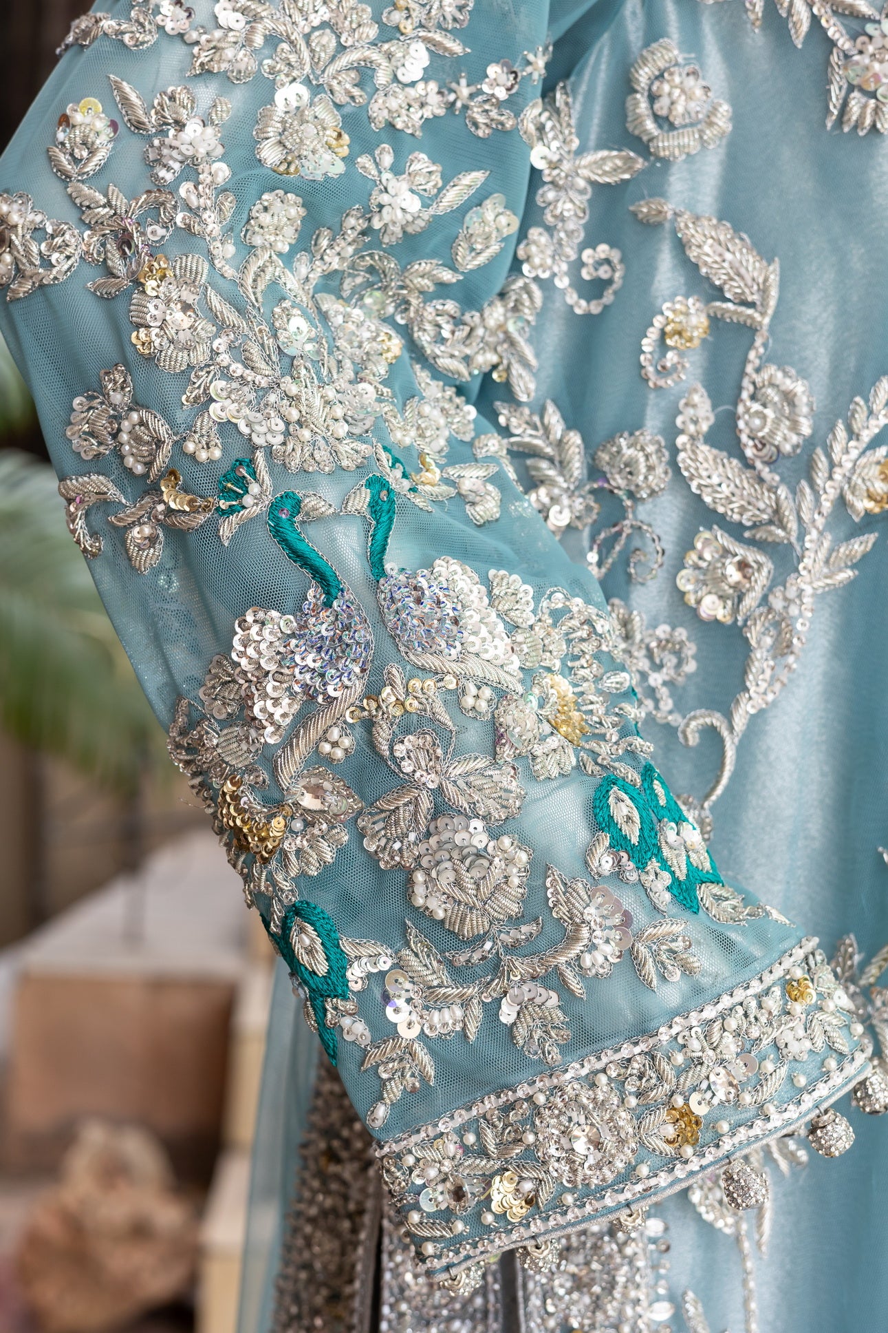 Teal Pakistani formal suit by MariamRaj featuring hand-embellished net shirt with zari, mirror work, pearls, and sequins, paired with tissue inner, embroidered pants, and a net dupatta.