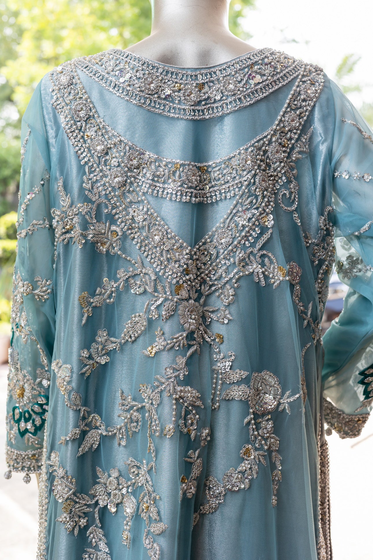 Teal Pakistani formal suit by MariamRaj featuring hand-embellished net shirt with zari, mirror work, pearls, and sequins, paired with tissue inner, embroidered pants, and a net dupatta.