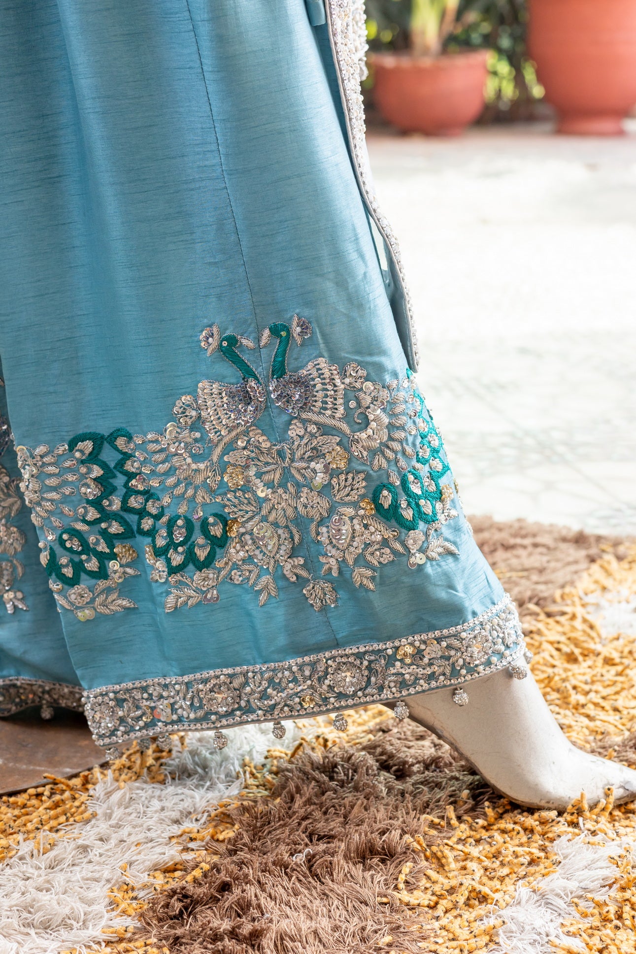 Teal Pakistani formal suit by MariamRaj featuring hand-embellished net shirt with zari, mirror work, pearls, and sequins, paired with tissue inner, embroidered pants, and a net dupatta.