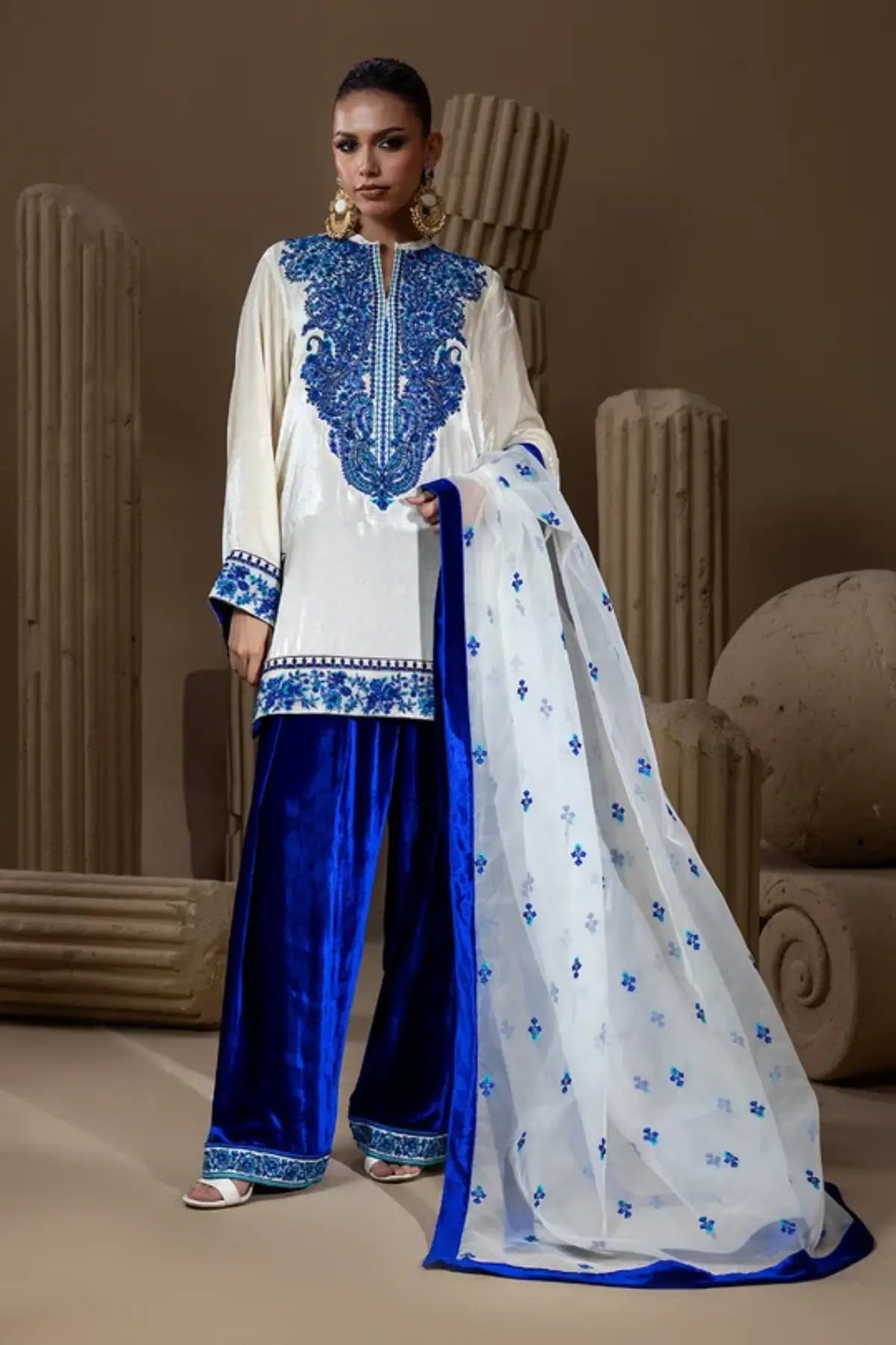 Neel Kamal ivory raw silk embroidered stitched suit with royal blue velvet Farshi shalwar and white organza dupatta with blue floral motifs.