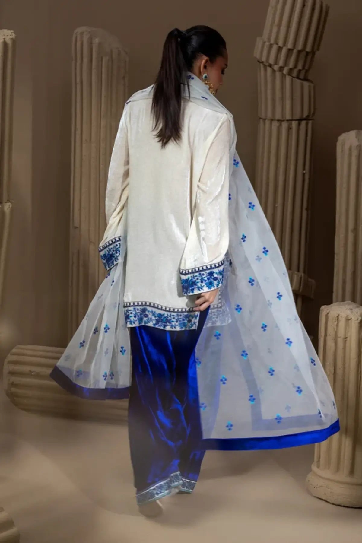 Neel Kamal ivory raw silk embroidered stitched suit with royal blue velvet Farshi shalwar and white organza dupatta with blue floral motifs.