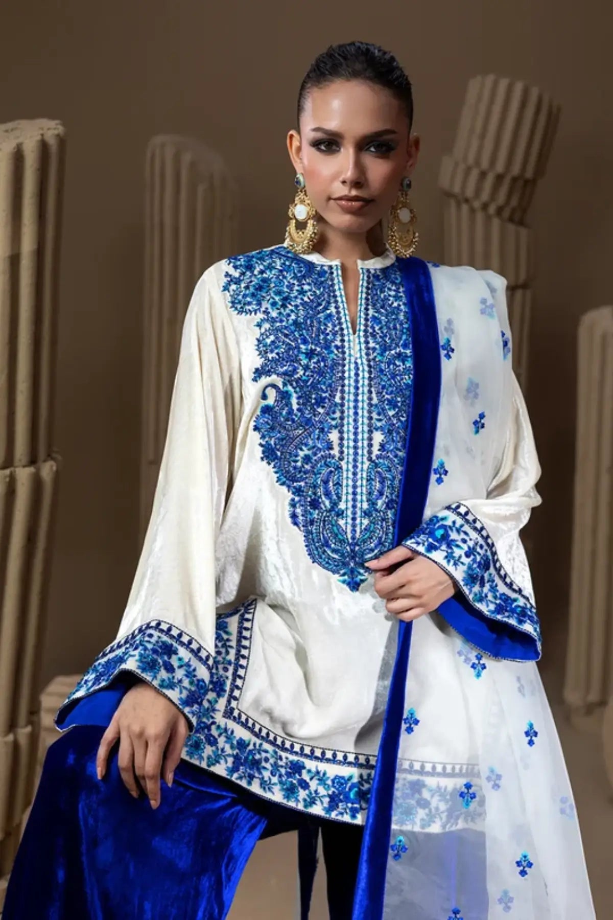 Neel Kamal ivory raw silk embroidered stitched suit with royal blue velvet Farshi shalwar and white organza dupatta with blue floral motifs.