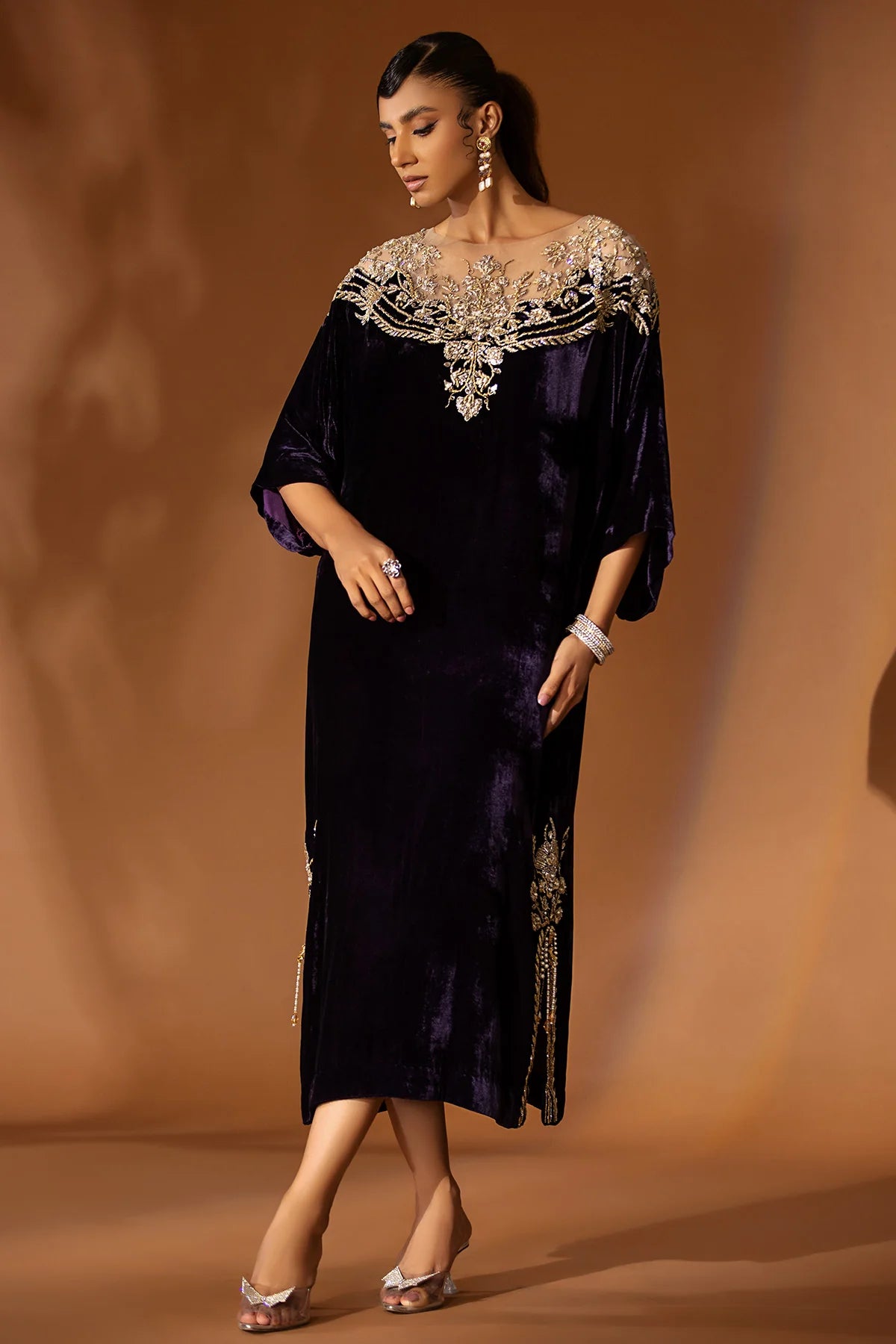 Purple velvet kaftan with embellished nude net neckline, short side slits, and gold jamawar pants with tissue finish – perfect for winter events 2025.

