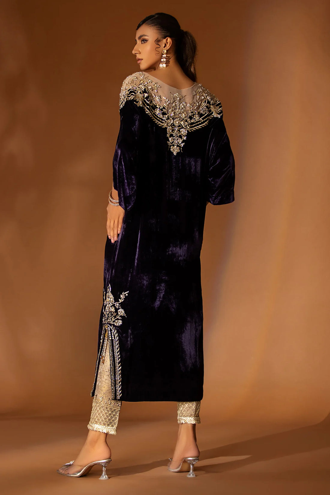 Purple velvet kaftan with embellished nude net neckline, short side slits, and gold jamawar pants with tissue finish – perfect for winter events 2025.

