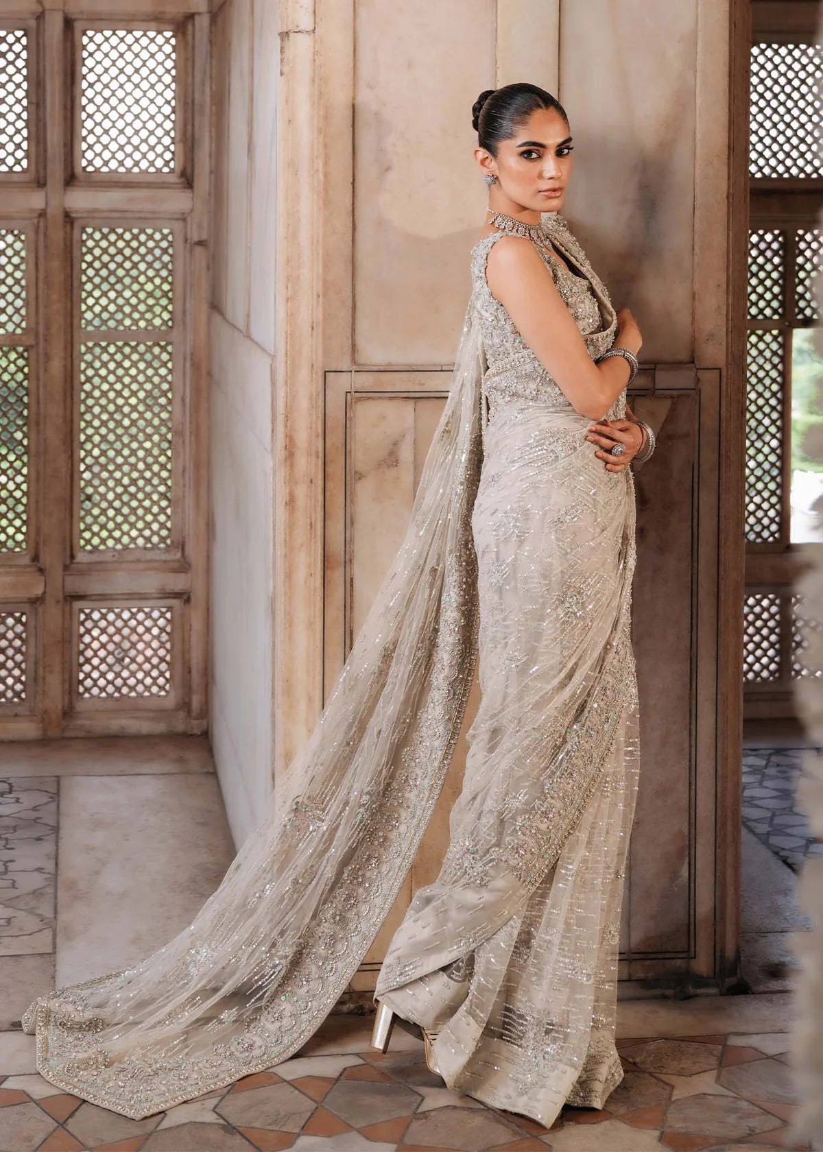 SIRAH – Ivory embroidered net saree with sequins, raw silk petticoat, and hand-embellished blouse. Stitched bridal saree online at Pakistanimoda.