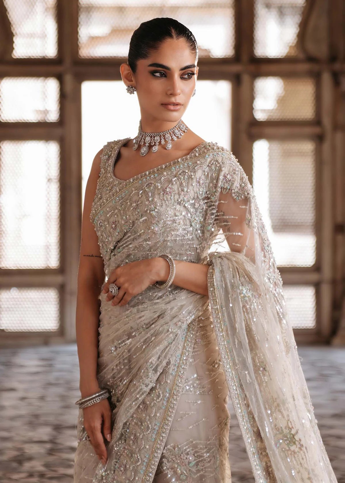 SIRAH – Ivory embroidered net saree with sequins, raw silk petticoat, and hand-embellished blouse. Stitched bridal saree online at Pakistanimoda.