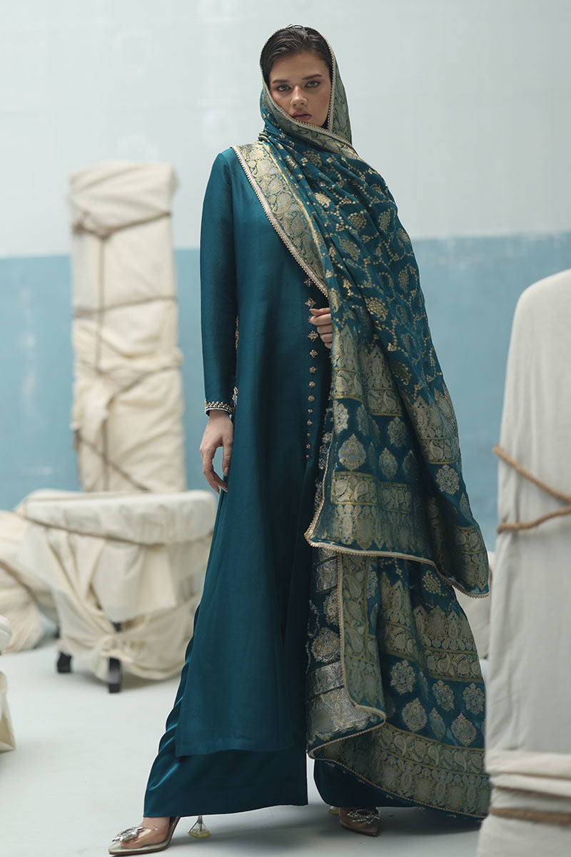 Peacock teal raw silk shirt with gold and silver zardozi, crepe silk culottes, and Banarasi chiffon dupatta – formal Pakistani ensemble for global events.